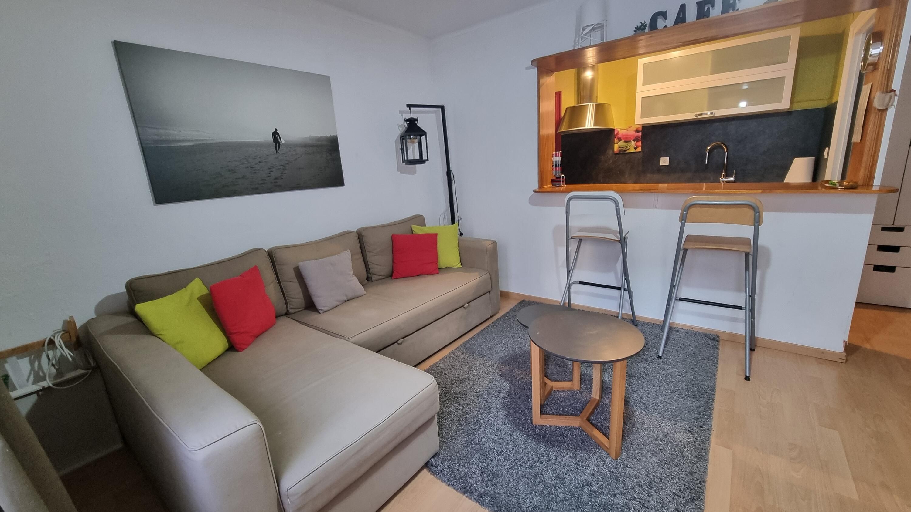 Un salon moderne comprenant un canapé, une petite table et un coin cuisine avec un comptoir et des chaises.
