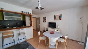 A compact living space with a kitchenette, a dining area with a round table and chairs, a TV, and a ceiling light fixture.