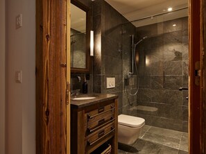 A modern bathroom with a wooden vanity, a toilet, and a glass-enclosed shower area.