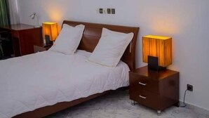 A neatly made bed with white bedding, two bedside tables with lamps, and a wooden headboard. - Residence Zety (Abidjan)