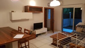 A compact living space with a dining table, a TV on a white cabinet, a sofa, and a balcony with a view of greenery. - Residence Zety (Abidjan)