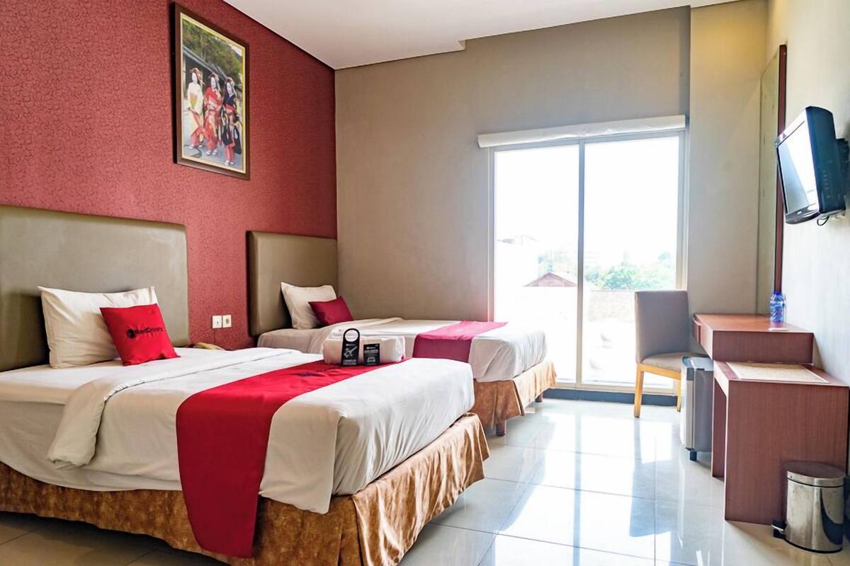 Habitación de hotel con dos camas, un escritorio, una silla, un televisor y una puerta corrediza de vidrio al exterior.