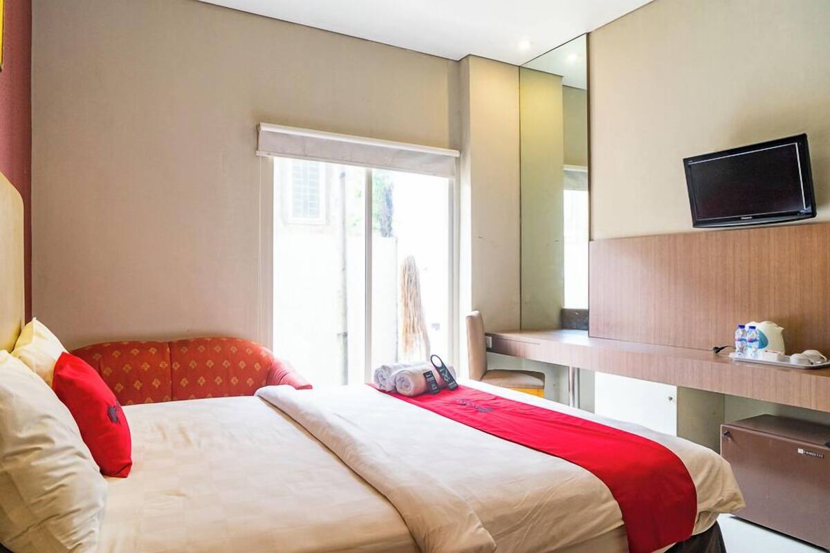 Una habitación de hotel con una cama, un escritorio, un televisor y una ventana.