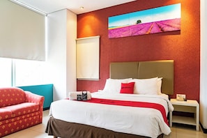 A hotel room with a bed, a red sofa, a nightstand, and a painting on the wall. - Reddoorz Plus Near Blok M Square (Jakarta)