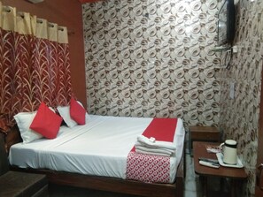 Un lit bien fait, avec une literie rouge et blanche, une tête de lit en bois et un mur à motifs derrière.
