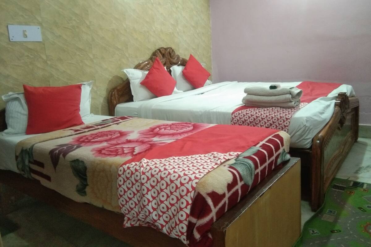 Habitación de hotel con dos camas, cada una con una colcha de cuadros rojos y blancos, cabeceros de madera y almohadas rojas.