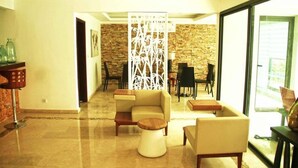 A modern living room with a sectional sofa, a round coffee table, and a dining area with a glass partition. - Villa Malis T6 (Abidjan)
