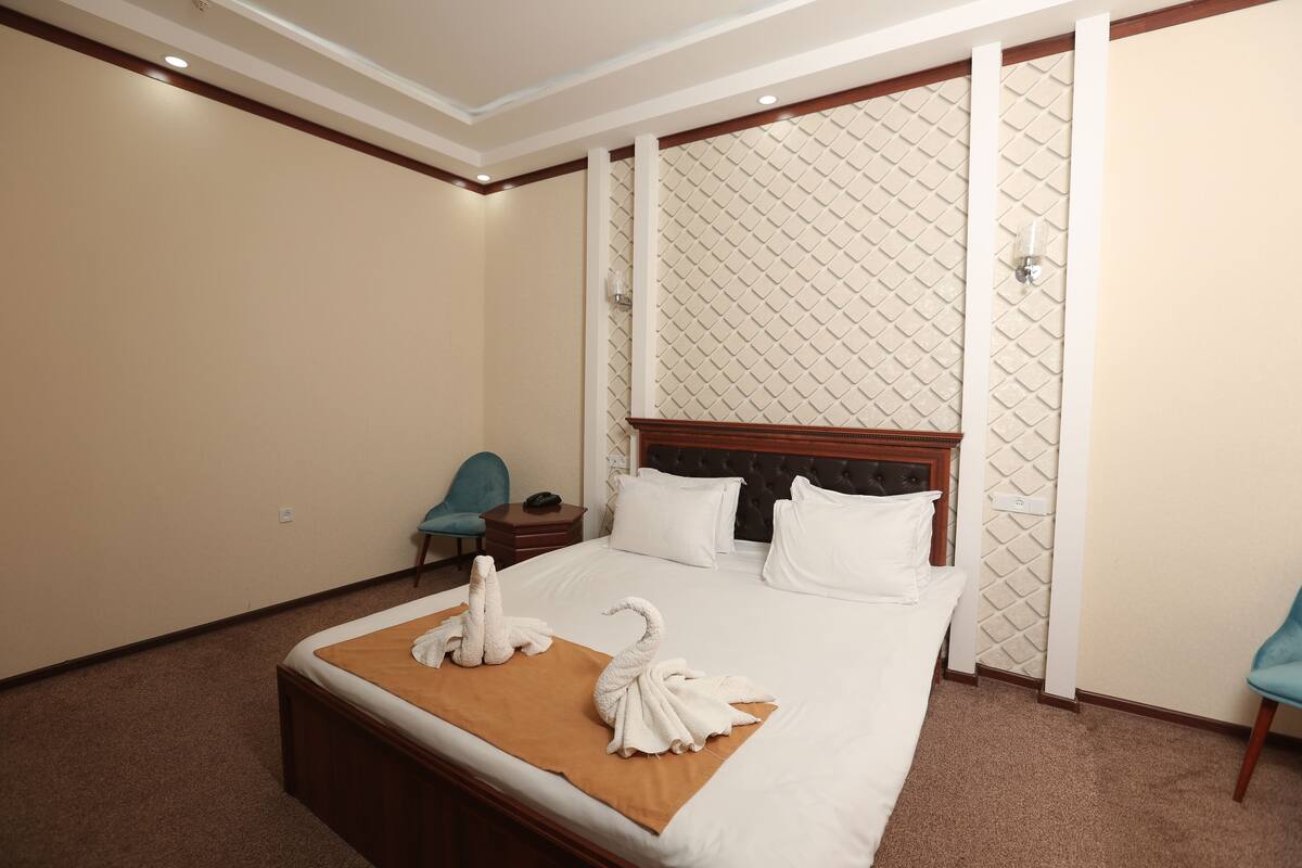 Habitación de hotel con una cama grande, cabecera de madera, una silla azul y una pared con diseño de rombos.