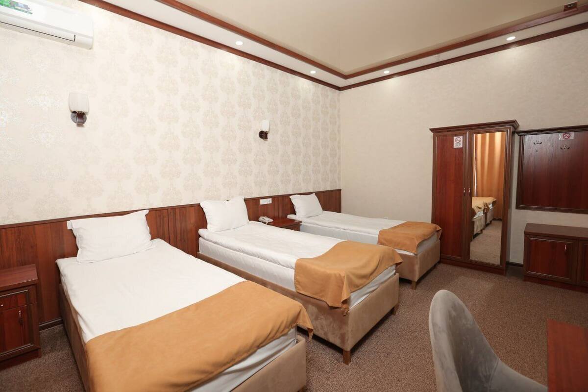 Habitación de hotel con tres camas individuales, cabeceros de madera, un armario de madera, un escritorio y una silla.