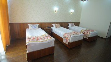 Habitación de hotel con tres camas de madera, cada una con un colchón blanco y almohadas decorativas. Hay dos lámparas de pared y una mesita de noche de madera con un teléfono.