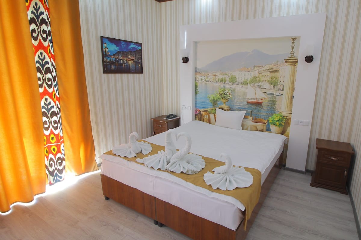 Habitación de hotel con cama, mesita de noche, escritorio y un gran mural de un paisaje urbano.