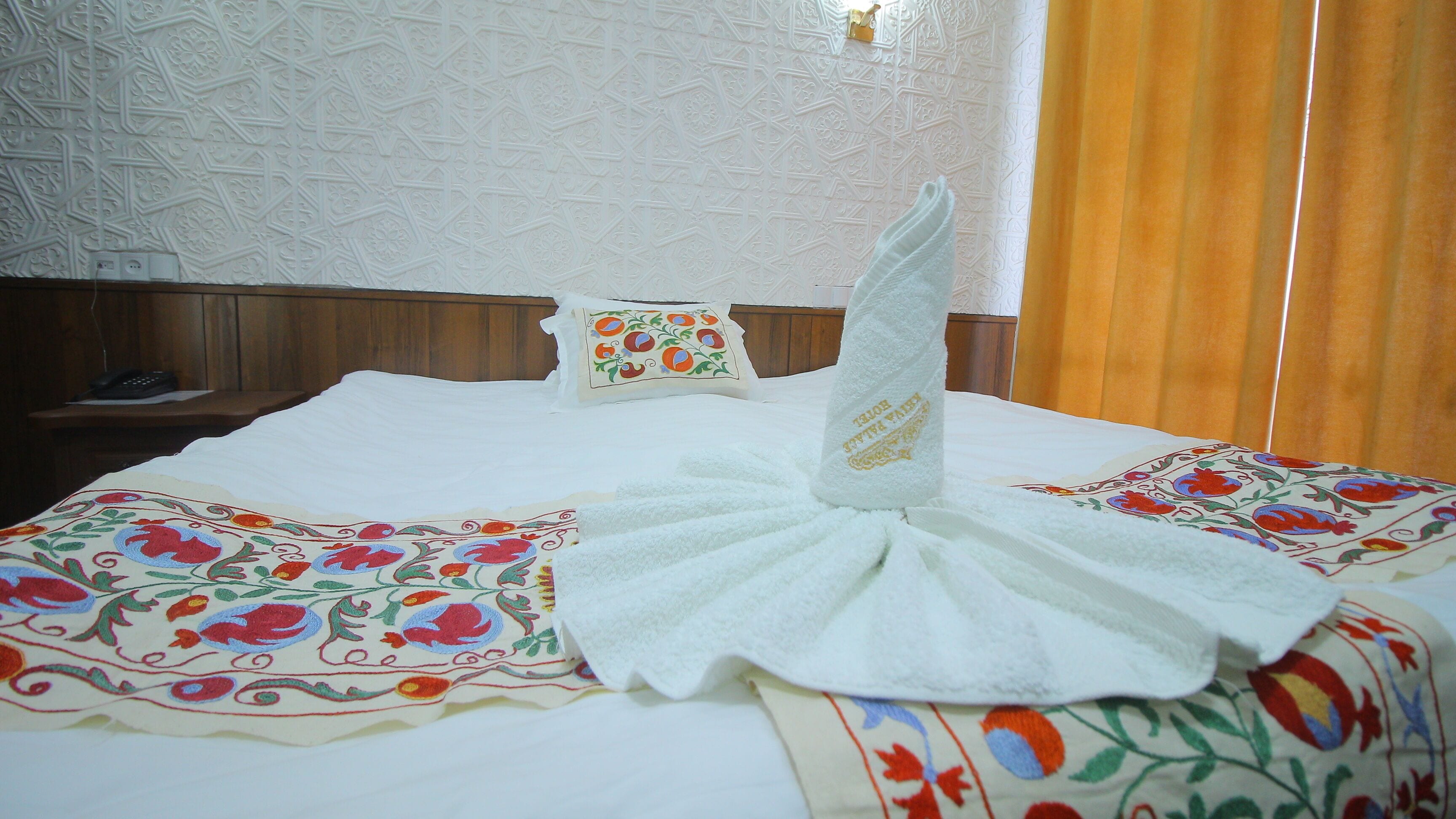Habitación de hotel con una cama bien hecha, cabecera de madera, almohada decorativa y colcha estampada.