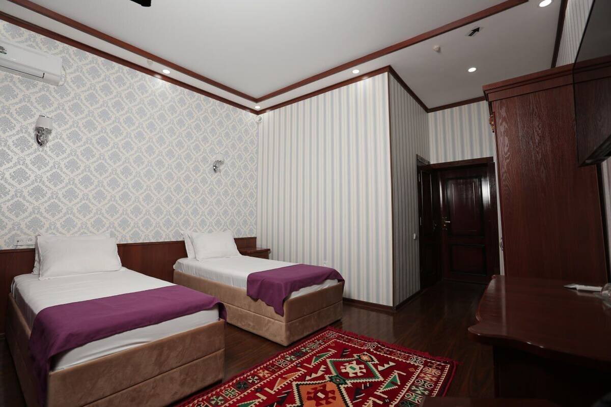 Habitación de hotel con dos camas, un escritorio de madera, un tapete estampado y una pared a rayas.