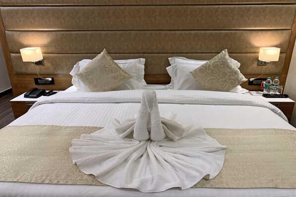 Habitación de hotel con una cama grande, dos lámparas de noche, un teléfono y una bandeja con agua embotellada y vasos.