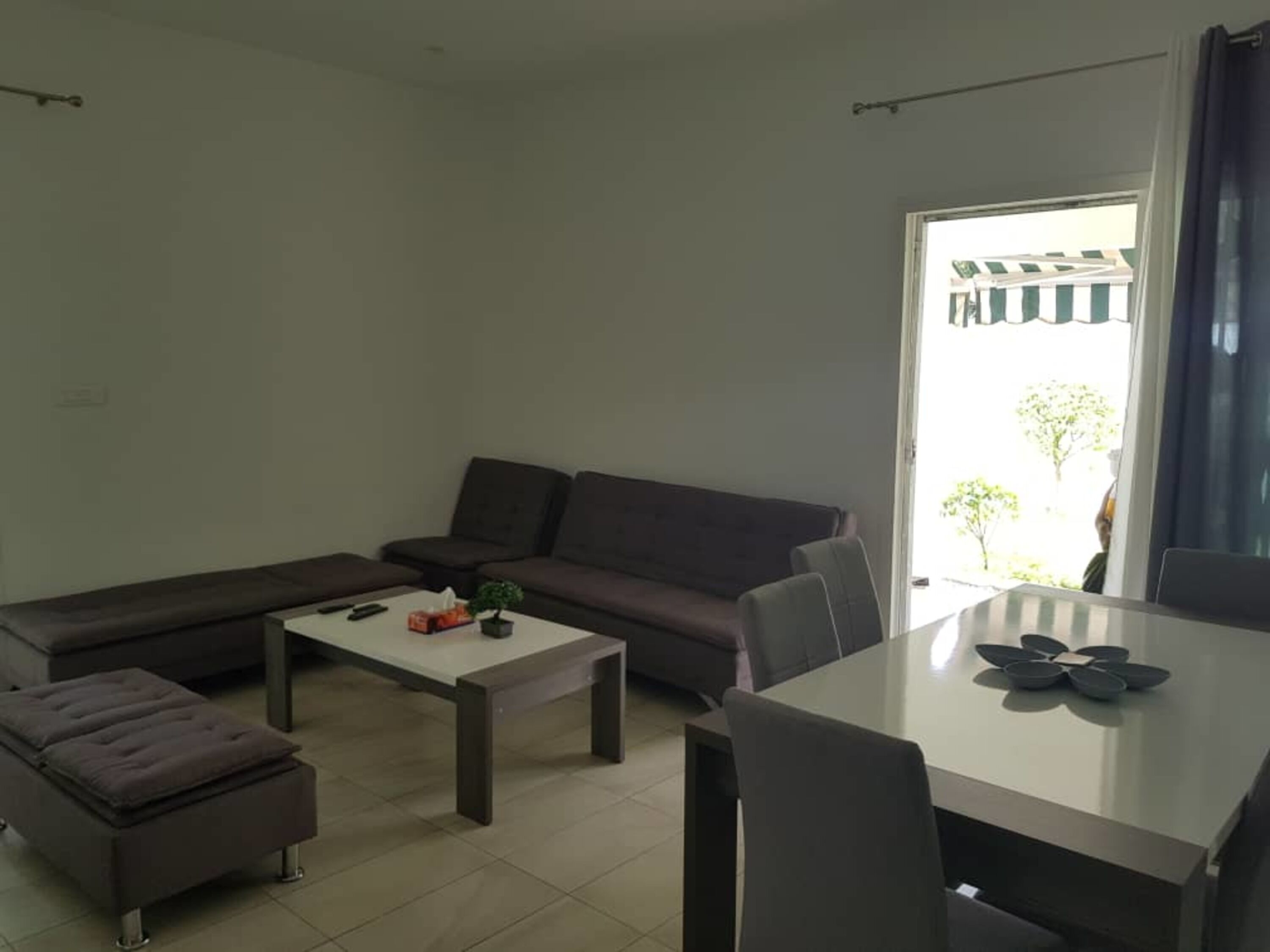 Ein modernes Wohnzimmer mit einem Ecksofa, einem kleinen Tisch und einem Essbereich mit weißem Tisch und Stühlen.