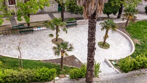 A courtyard with palm trees, benches, and a stone building in the background. - Gorgeous and Spacious Apartment Equipped with Unique and Valuable Furniture  (Split)