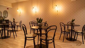 Un comedor con mesas y sillas redondas, luminarias fijadas a la pared y plantas en macetas.