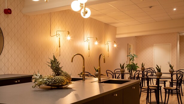A modern kitchen with a central island, stainless steel appliances, and a dining area with wooden tables and chairs. - Hotell Syfabriken (Falkoping)