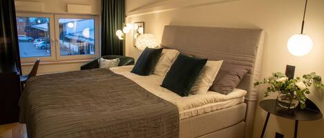 A bedroom with a large bed, a desk, and a window with curtains.