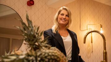 A person standing in a room with a pineapple on the counter, a gold faucet, and a patterned wall.