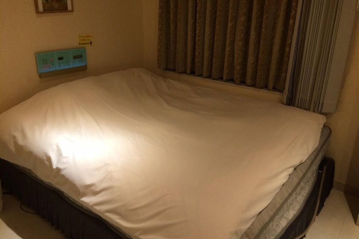 A single bed with a white mattress and dark headboard in a room with beige walls.