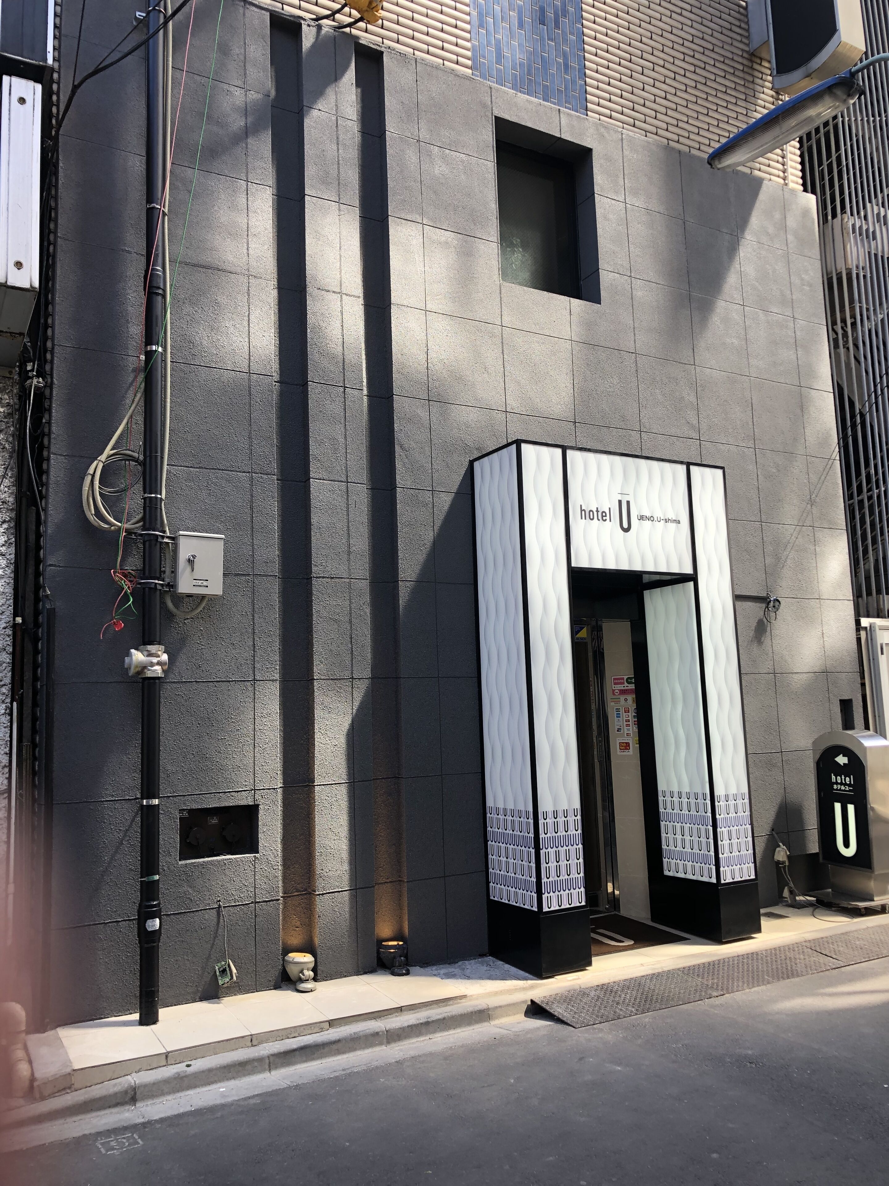 A hotel entrance with a modern design, a visible door, and a sign indicating the hotel name.