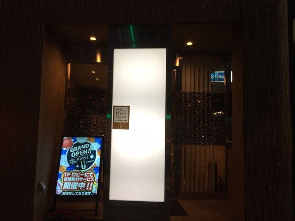A hotel entrance with a sign indicating free Wi-Fi and a digital display advertising a grand opening. - Hotel U (Tokyo)