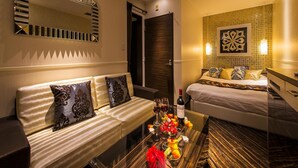 A hotel room with a sofa, a bed, a glass coffee table with flowers, and a wall with a decorative pattern.