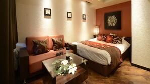 A hotel room with a bed, a sofa, a glass coffee table, and a wall-mounted lamp.