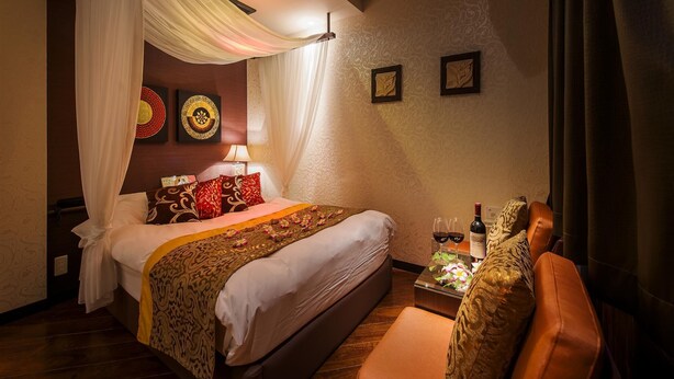 A hotel room with a bed, a bedside table with a bottle and glasses, a chair, and a canopy bed.