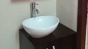 A bathroom with a white sink, a wooden-framed mirror, and dark cabinets. - Residence Mturquoise T1 (Abidjan)