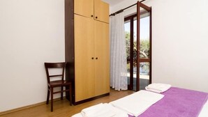 Een slaapkamer met een houten garderobe, een stoel, een bed met een paars dekbed en een uitzicht op de omgeving door een glazen deur.