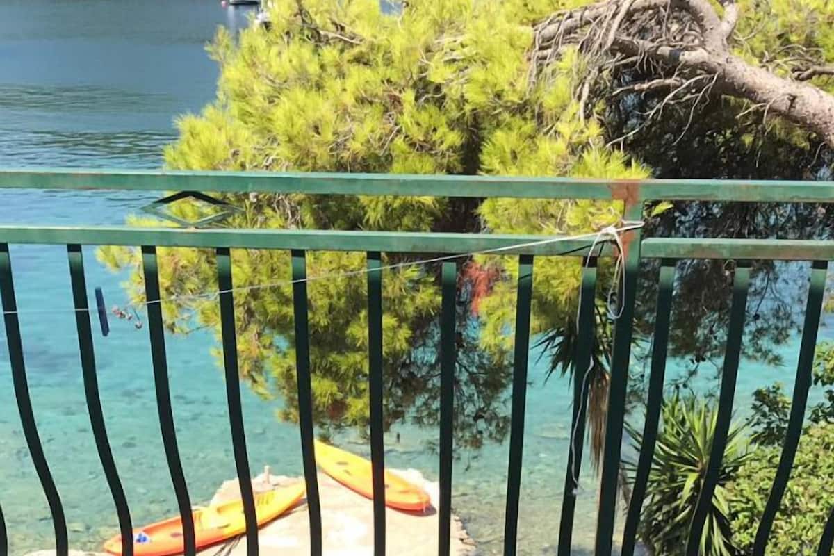 Un balcón con vista a un lago azul y despejado, un árbol y un kayak.