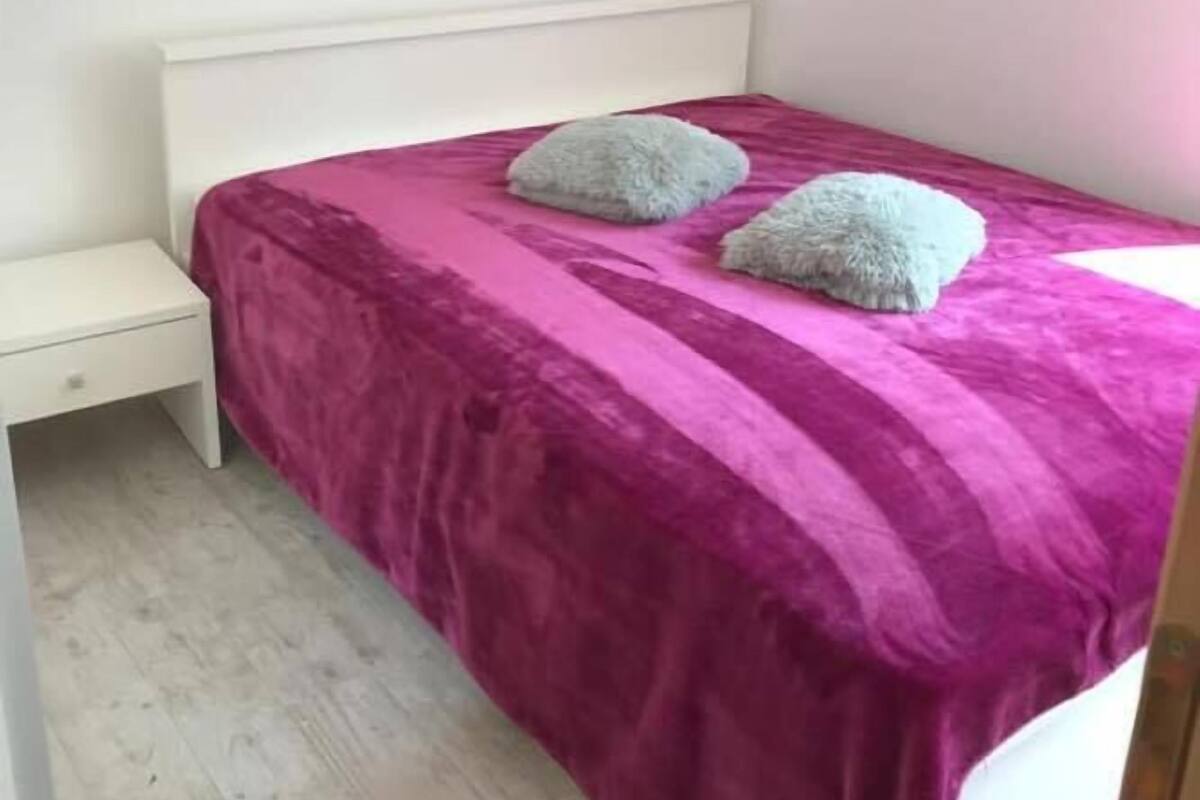Un dormitorio con una cama cubierta con un edredón púrpura, dos almohadas y una mesita de noche blanca.