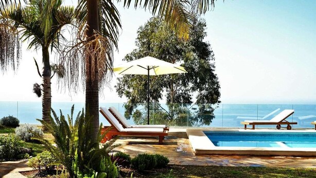 A poolside area with lounge chairs and an umbrella, surrounded by tropical plants and a view of the ocean. - Perseidas House, Wonderfull house with pool and sea views. (Tijarafe)