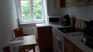 A small kitchen with a window, a microwave, a kettle, and a table with chairs. - Apartments Sachsenallee (Chemnitz)