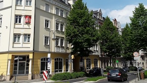 A multi-story building with a yellow facade, large windows, and a prominent entrance. - Apartments Sachsenallee (Chemnitz)