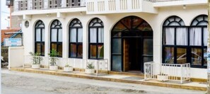 Un hotel con fachada blanca, varios ventanales de arco y un balcón con macetas.