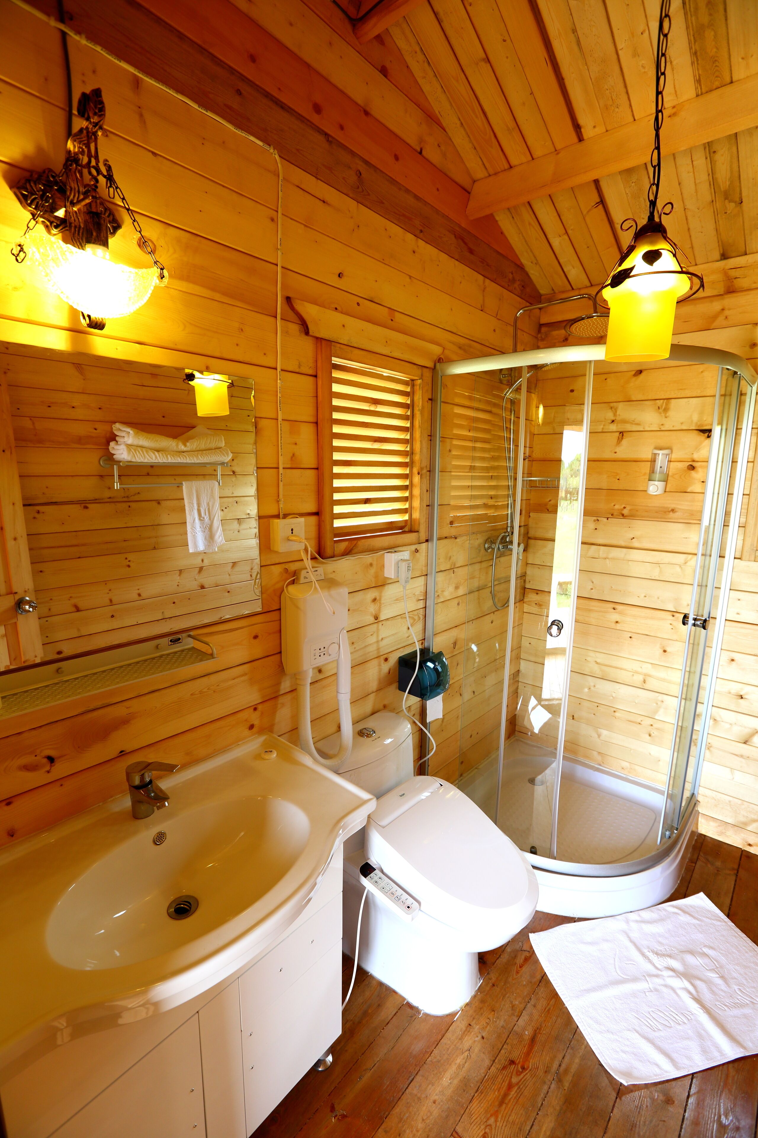 A wooden cabin bathroom with a sink, toilet, and glass-enclosed shower.
