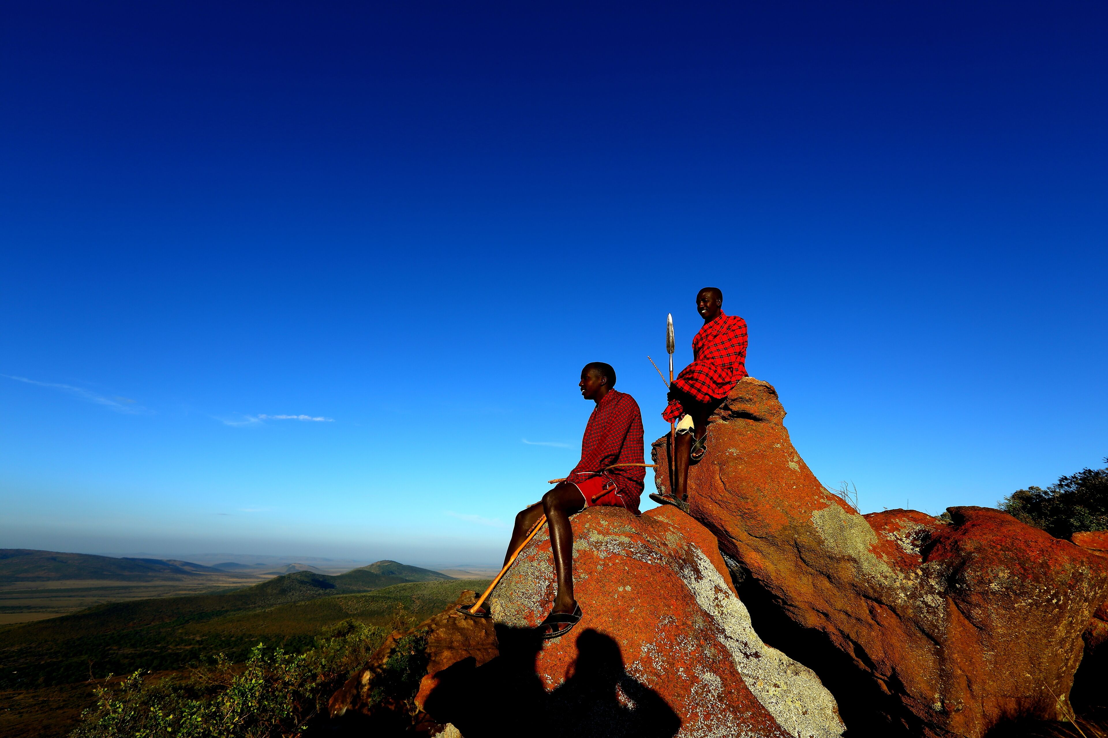 Dos personas sentadas sobre una roca grande con una vista panorámica del paisaje.