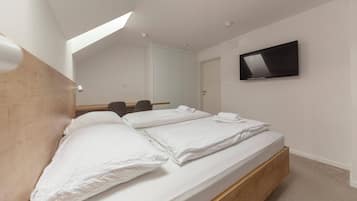 A bedroom with two beds, a TV mounted on the wall, and a skylight.