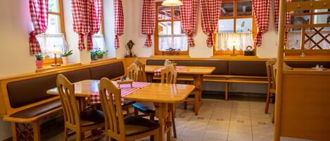 A cozy restaurant with wooden furniture, checkered curtains, and hanging lamps.
