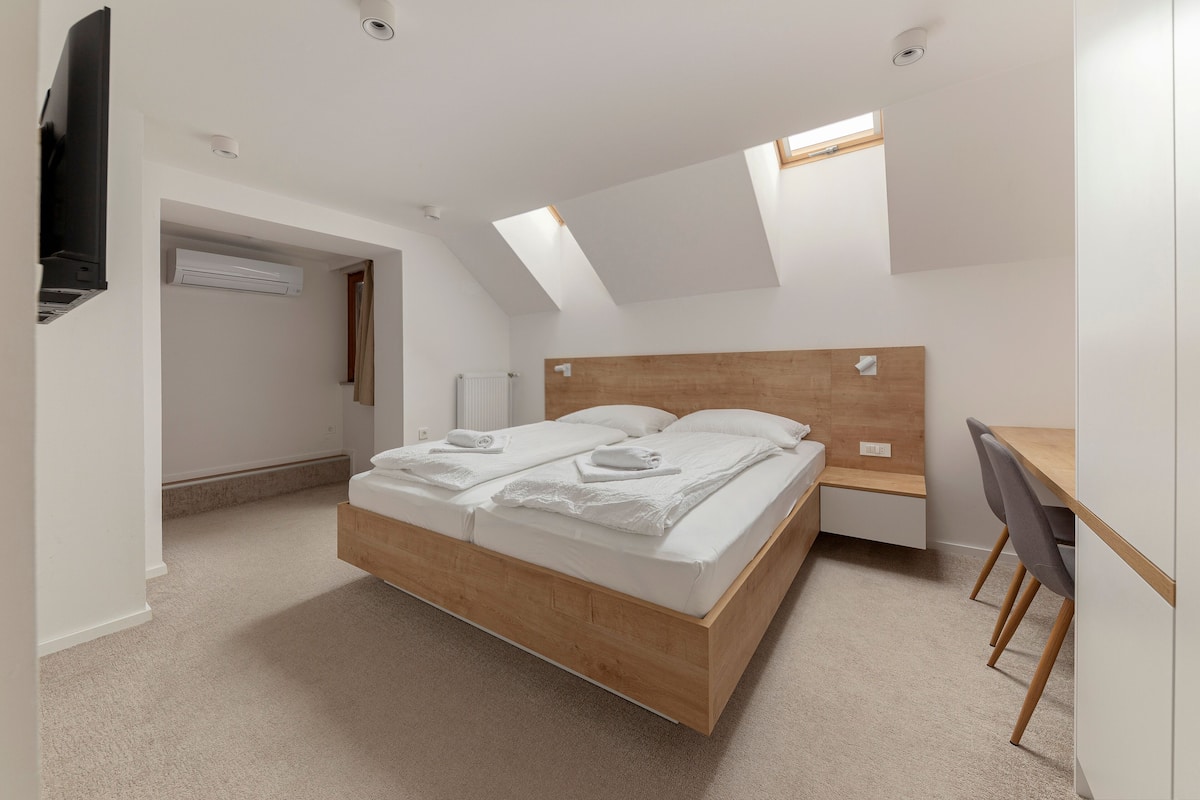 Quarto moderno com cama de madeira, escrivaninha e claraboia.