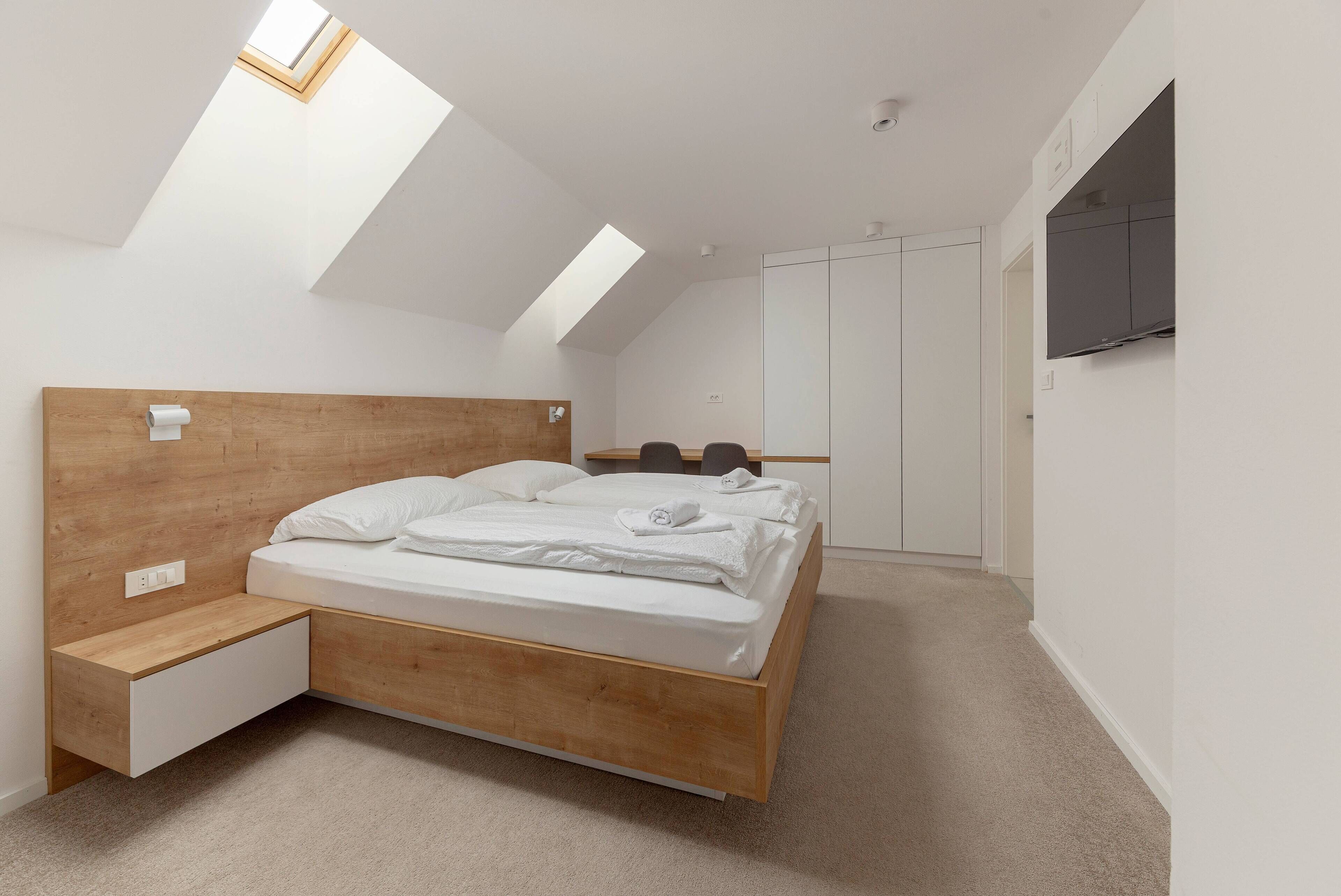 Una camera da letto con un letto in legno, un comodino, un armadio e un lucernario.