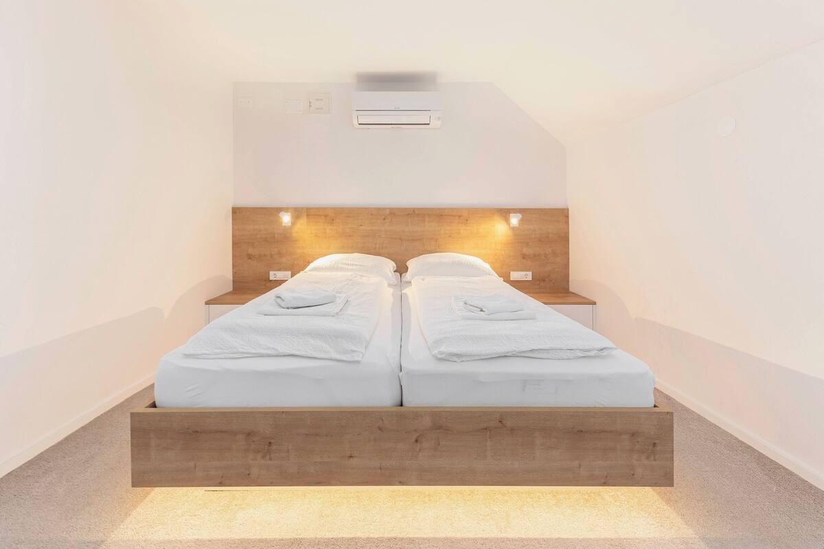 Um quarto moderno com cabeceira de madeira, duas camas com roupa de cama branca e abajures.