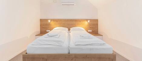 Un dormitorio moderno con cabecera de madera, dos camas con ropa blanca y lámparas de noche.