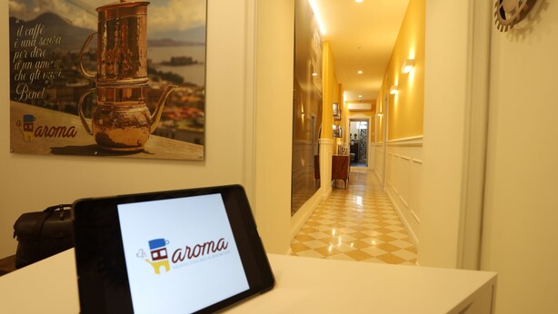 Una tableta mostrando el logo 'aroma' en un pasillo con piso a cuadros, un cartel de una cafetera y una pared con un diseño de engranaje.