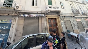Un edificio de varios pisos con balcones, una entrada a nivel de calle y un automóvil estacionado.