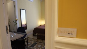 Una habitación de hotel con cama, escritorio con un florero, espejo y un letrero que dice "ROBUSTA ROOM".