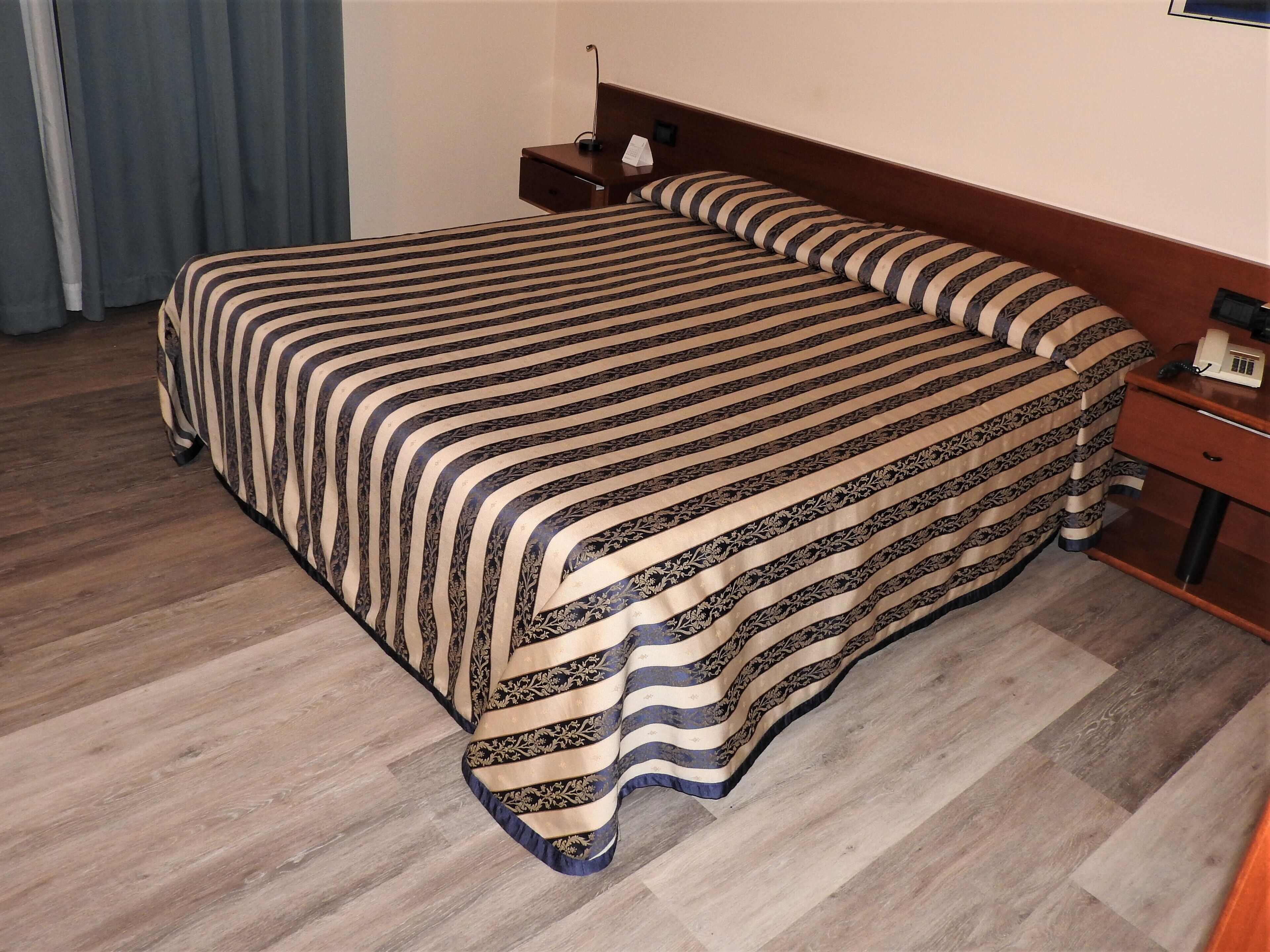 A hotel room with a large bed, a nightstand, a lamp, and a telephone.